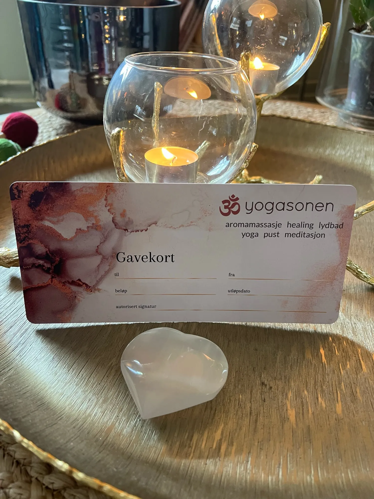 Trykket gavekort fra Yogasonen på et messingbrett med levende lys og et hjerte av krystall