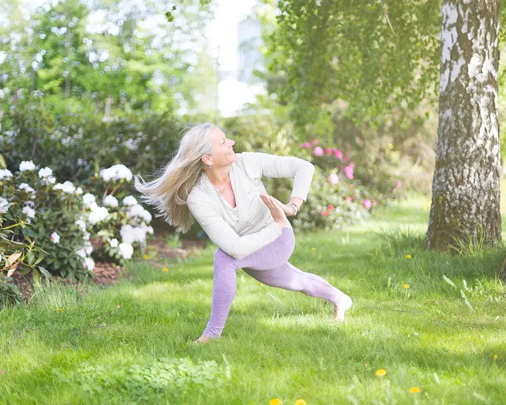 Wenche i en stående yogastilling i en grønn hage